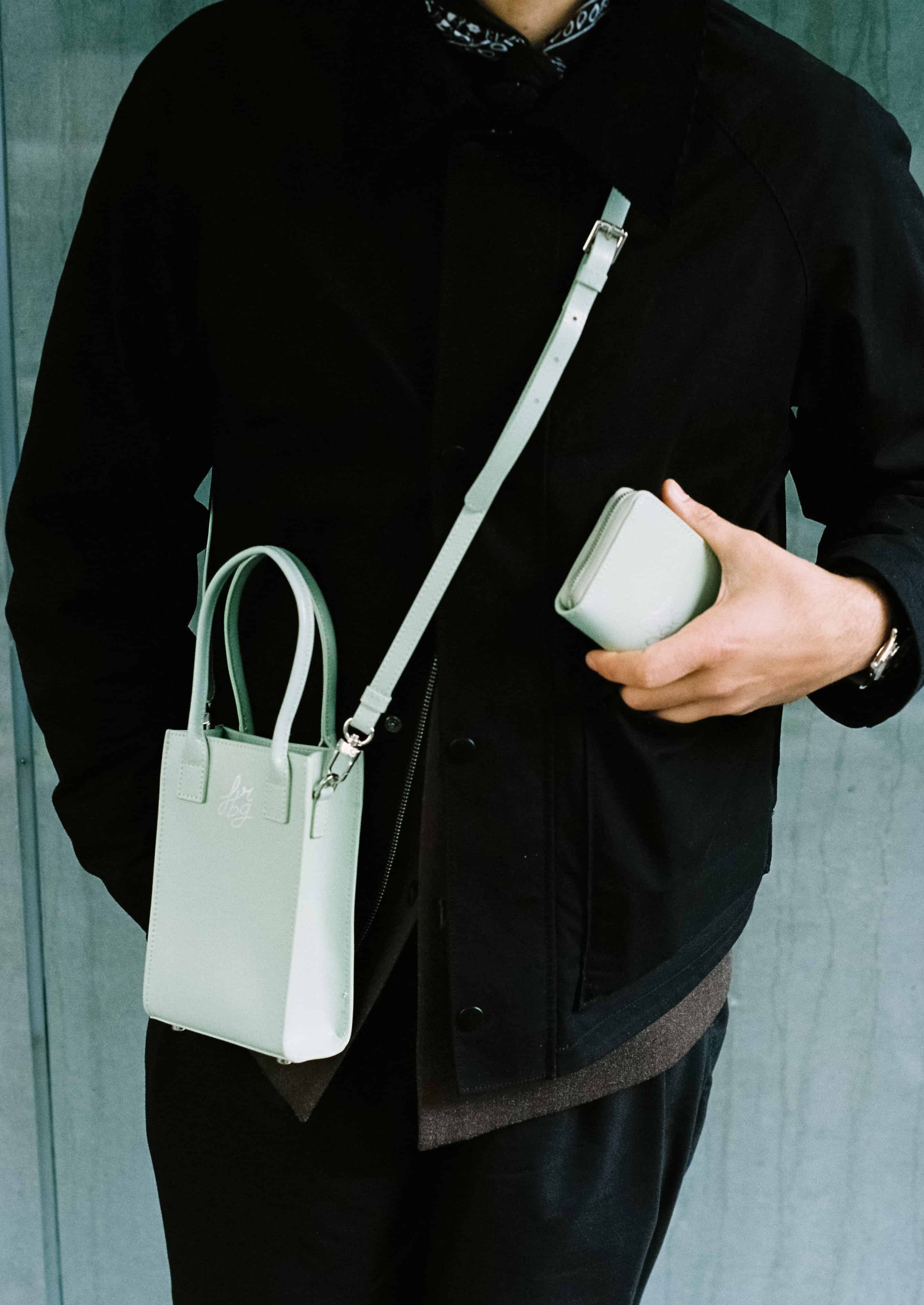 Personne en noir avec un sac et un portefeuille verts clairs