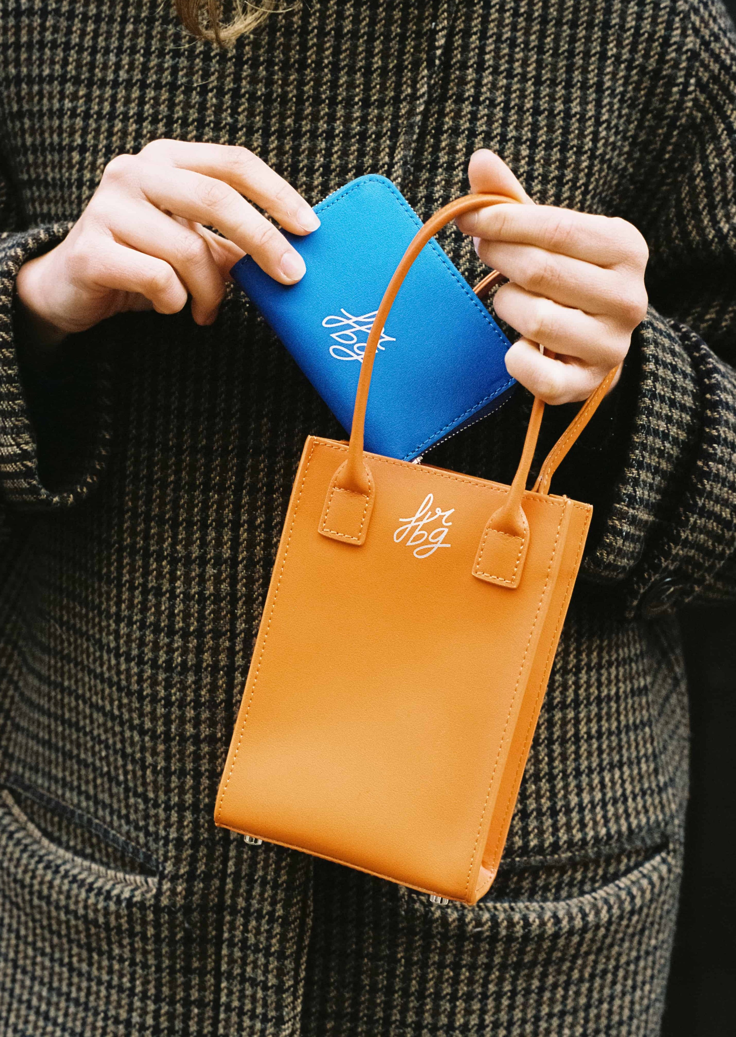 Main tenant un porte-monnaie bleu et un sac orange
