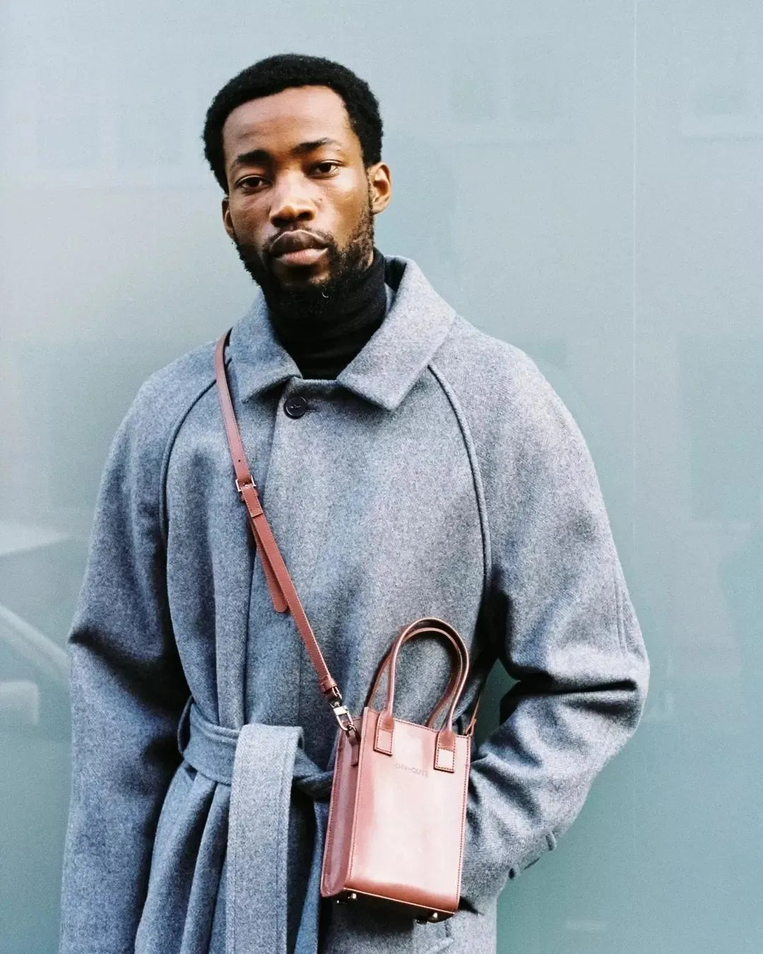 Un homme portant un manteau gris avec un petit sac marron