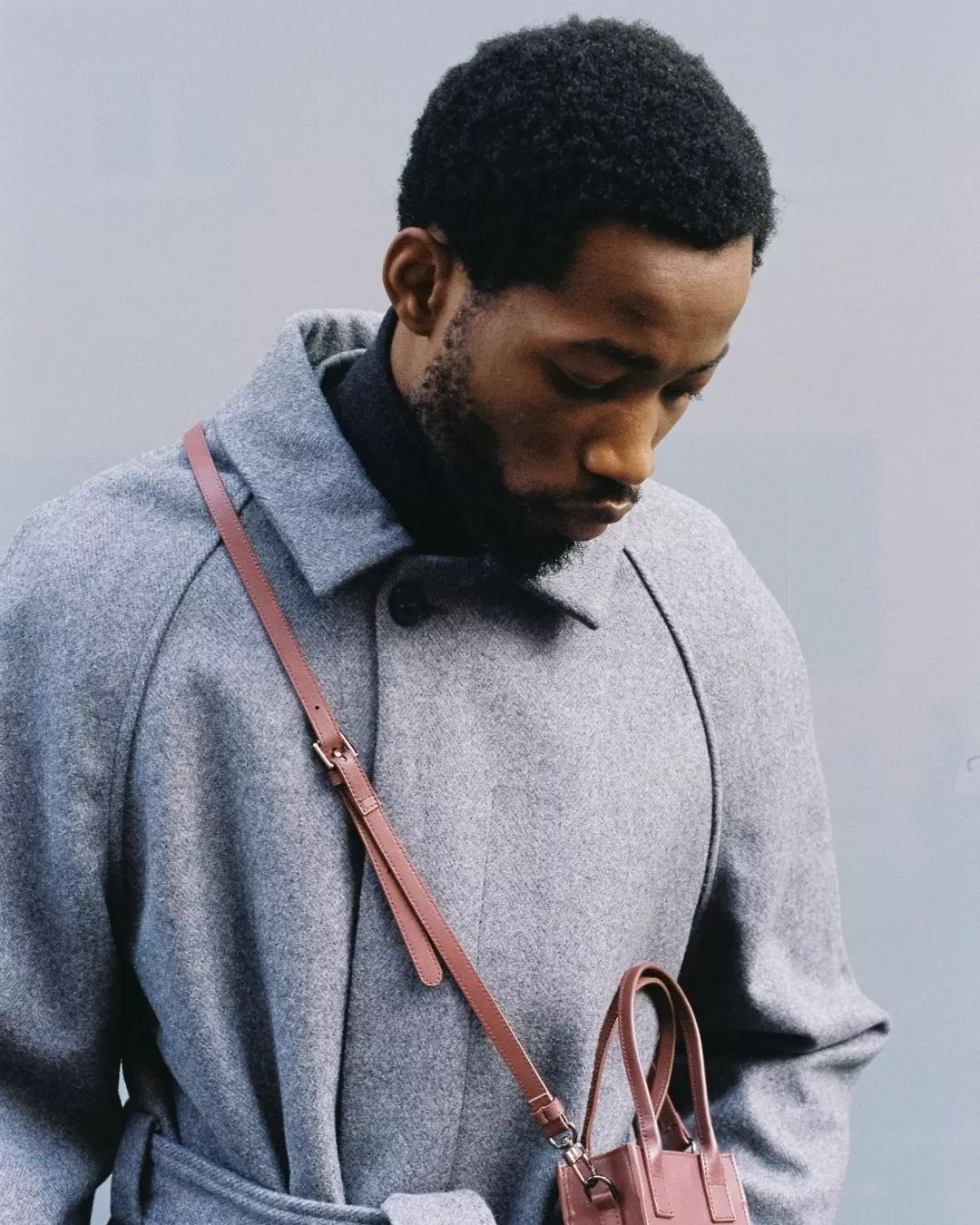 Un homme portant un manteau gris avec un petit sac marron