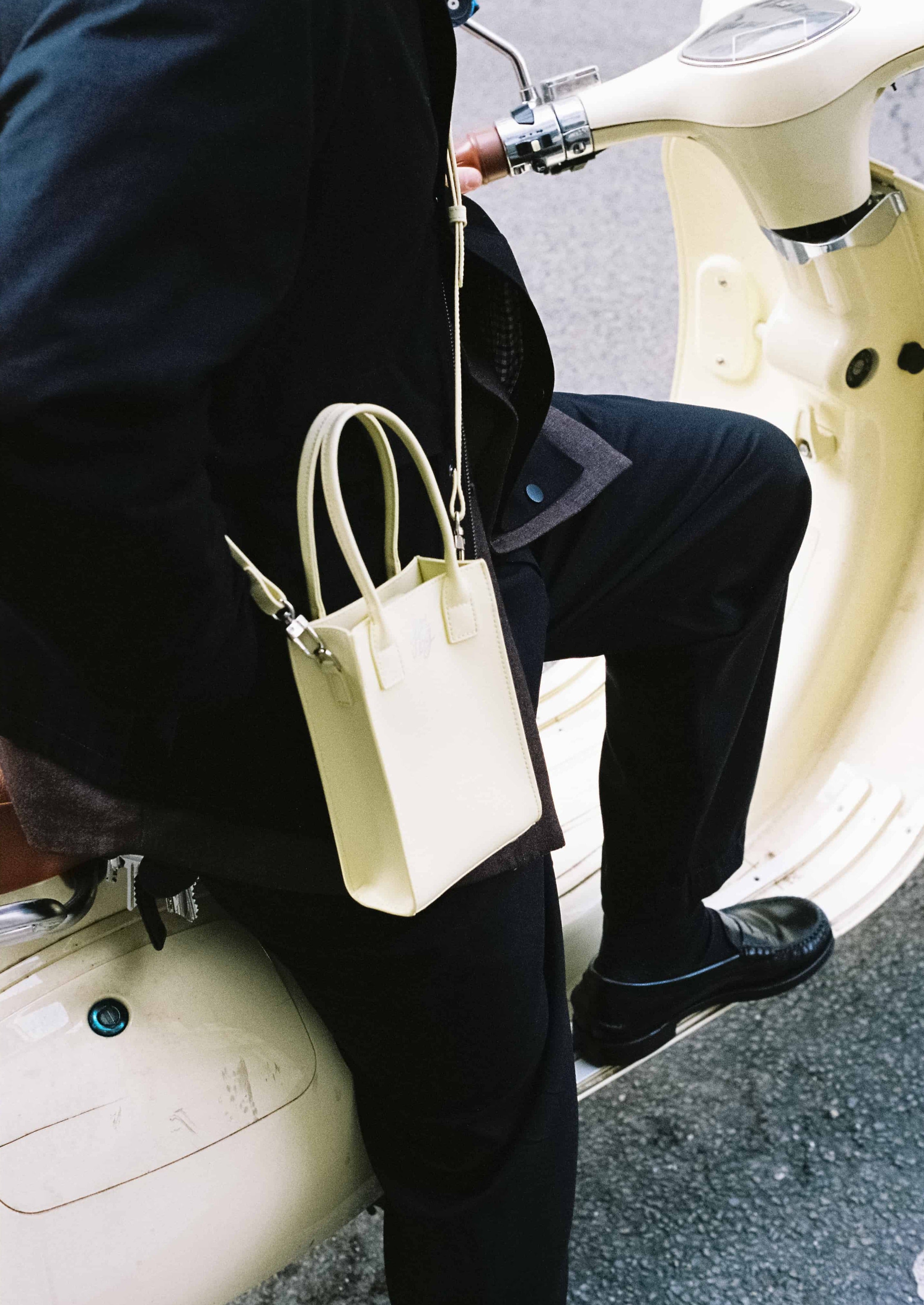 Homme en noir assis sur un scooter, portant un sac jaune pastel