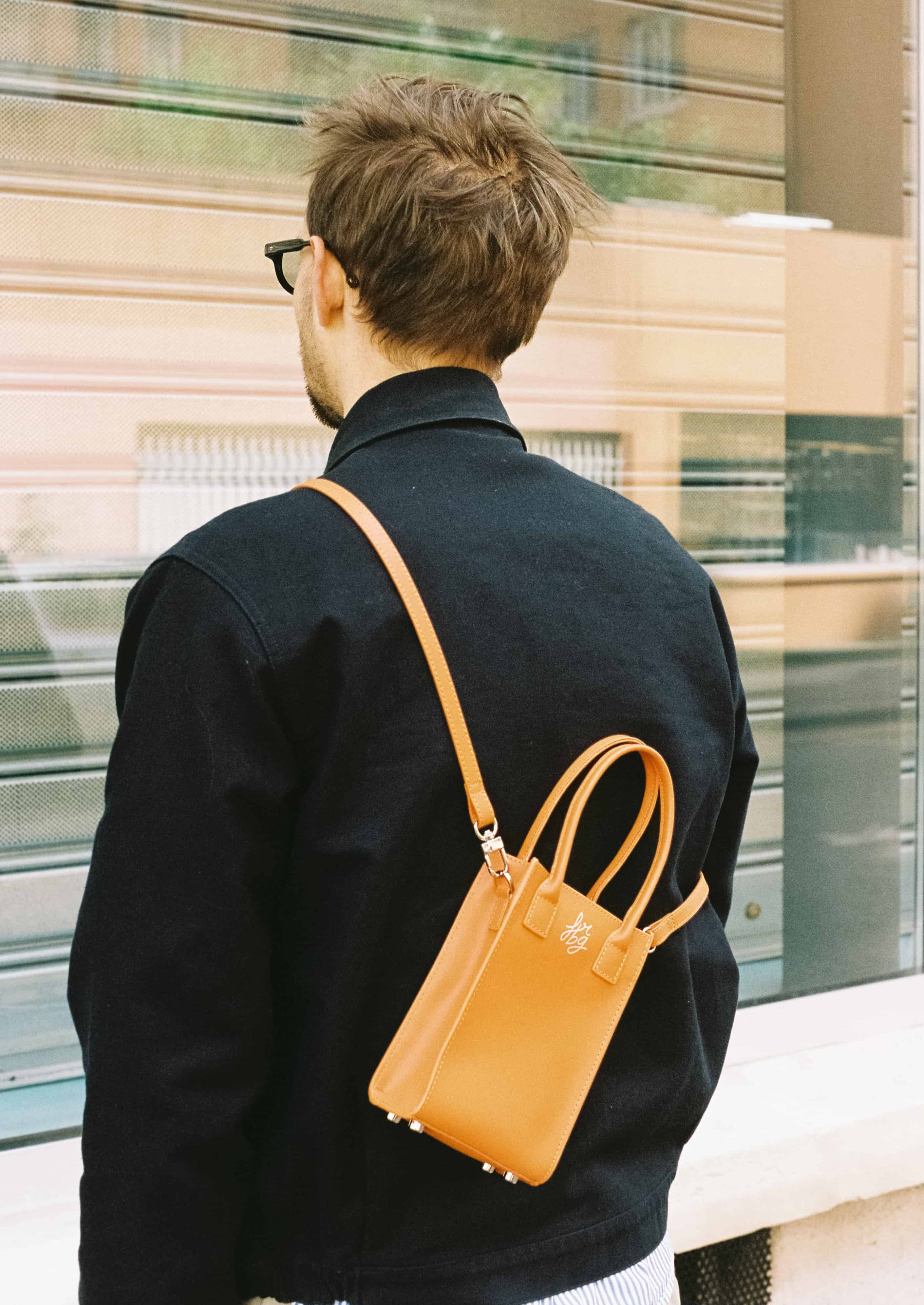 Homme de dos avec sac orange en bandoulière et lunettes