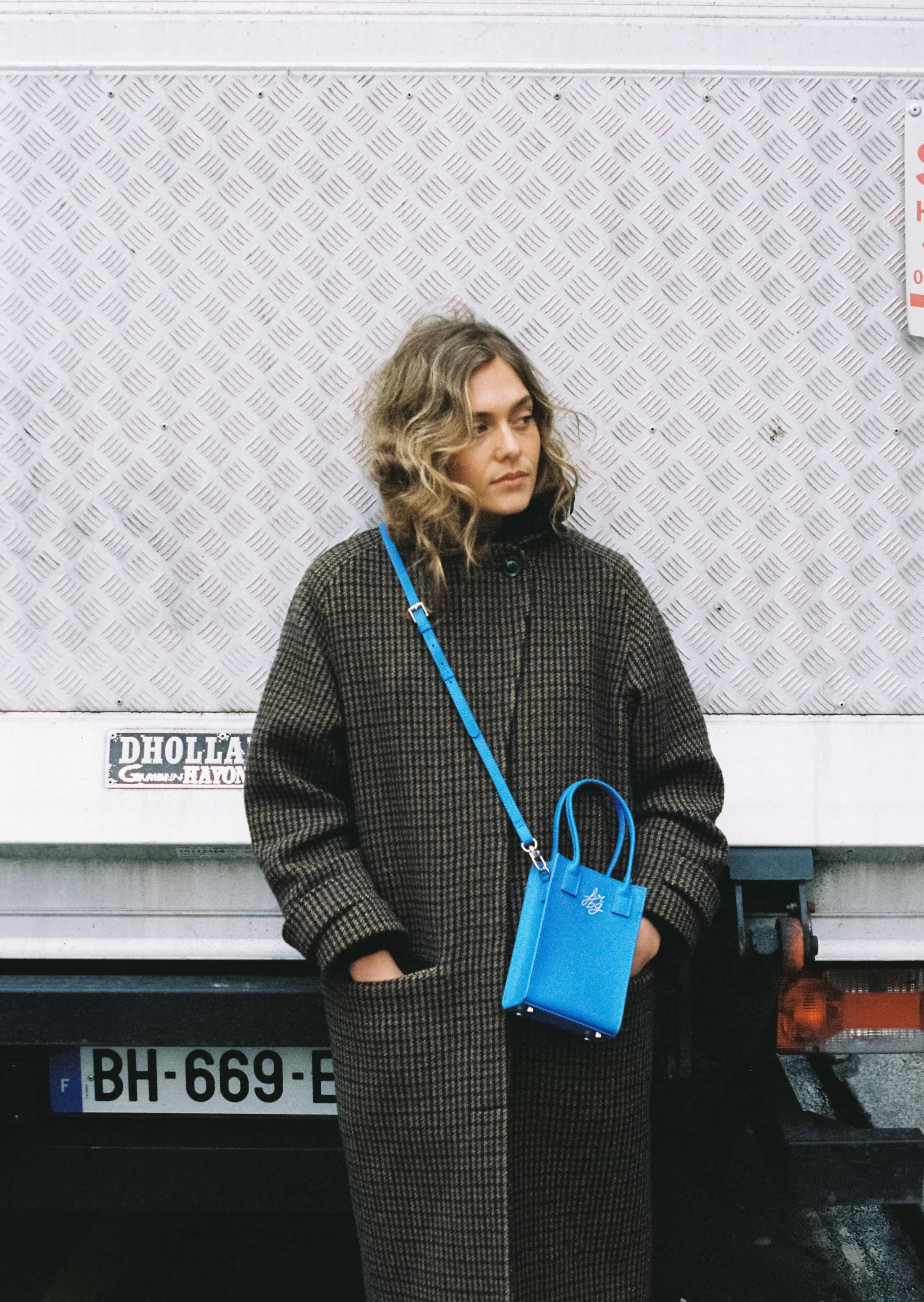 Femme en manteau à carreaux avec sac bleu à bandoulière
