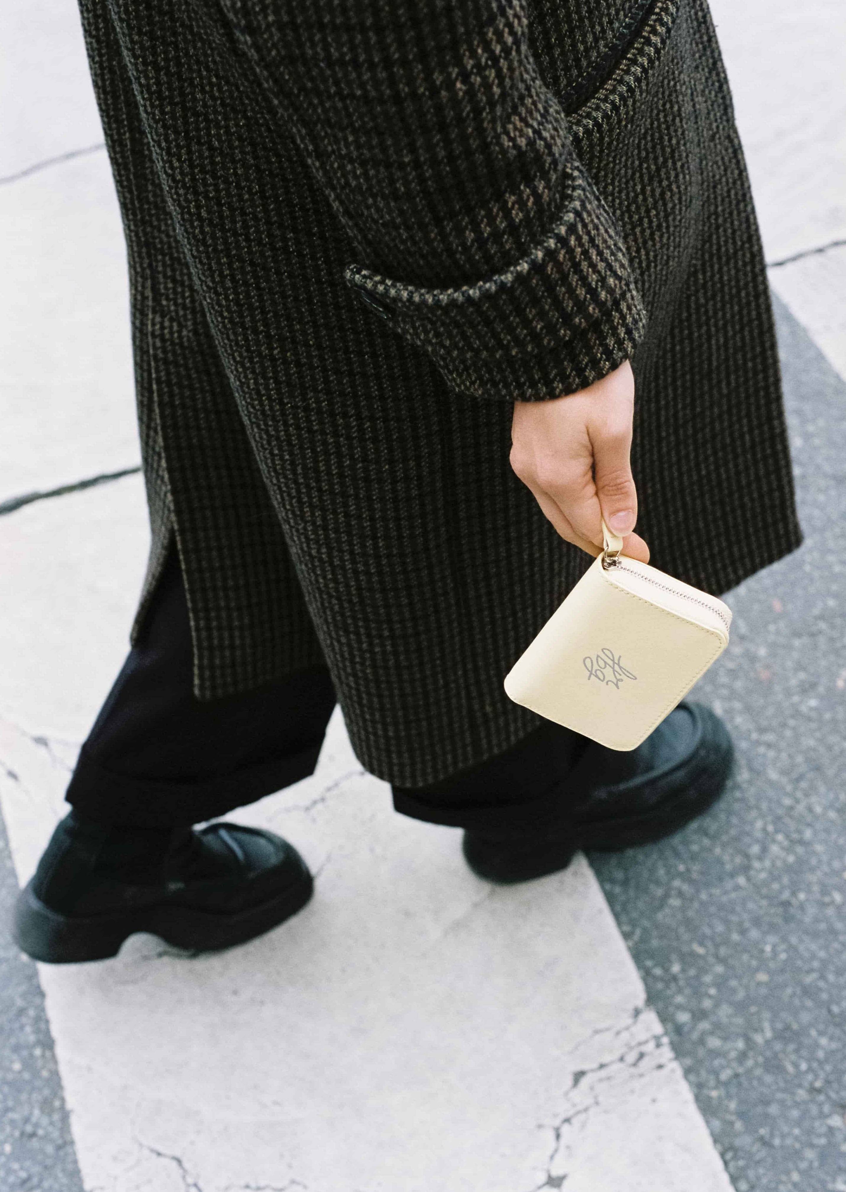 Personne marchant avec un manteau foncé et un portefeuille jaune pastel