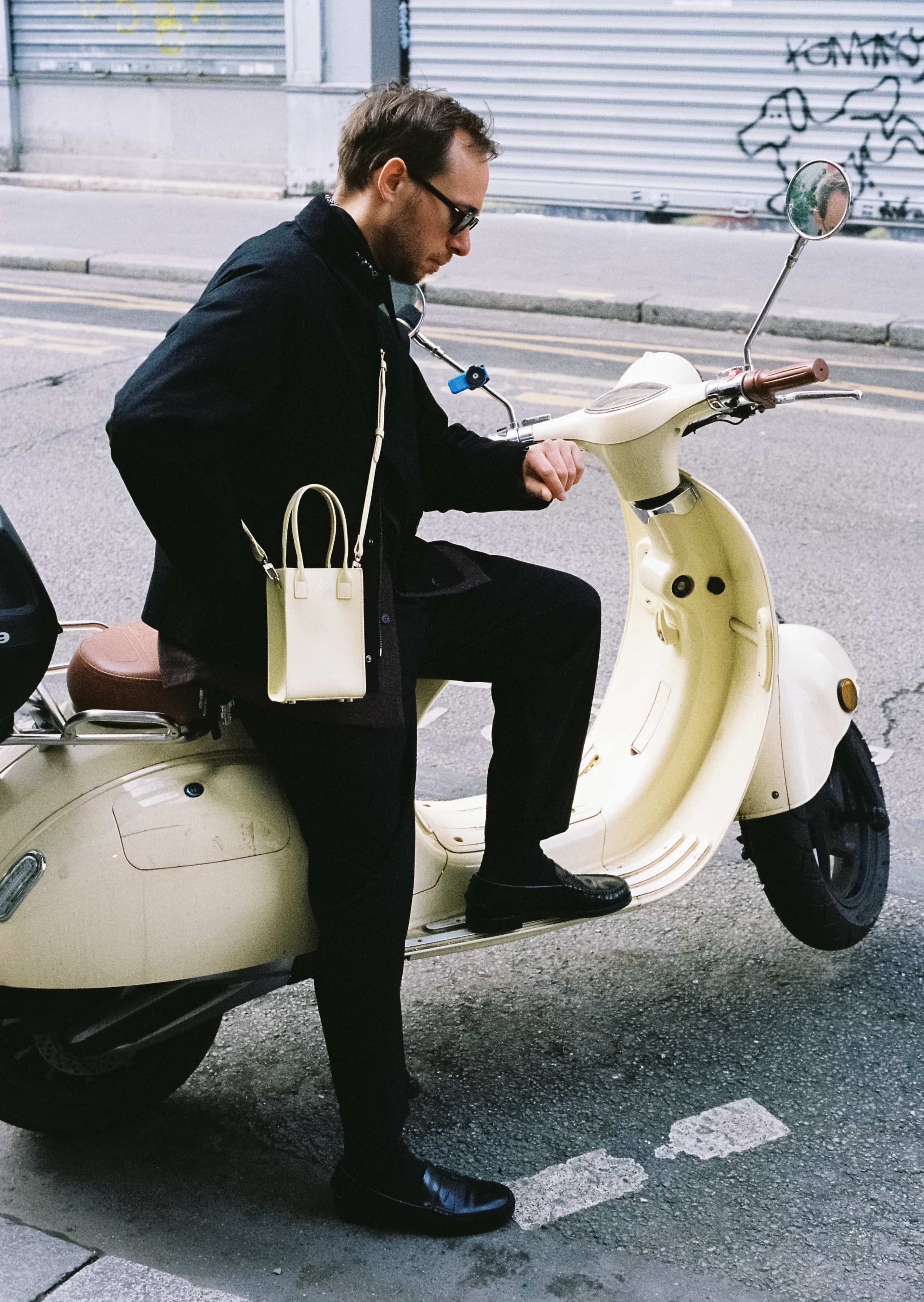 Homme en noir assis sur un scooter, portant un sac jaune pastel