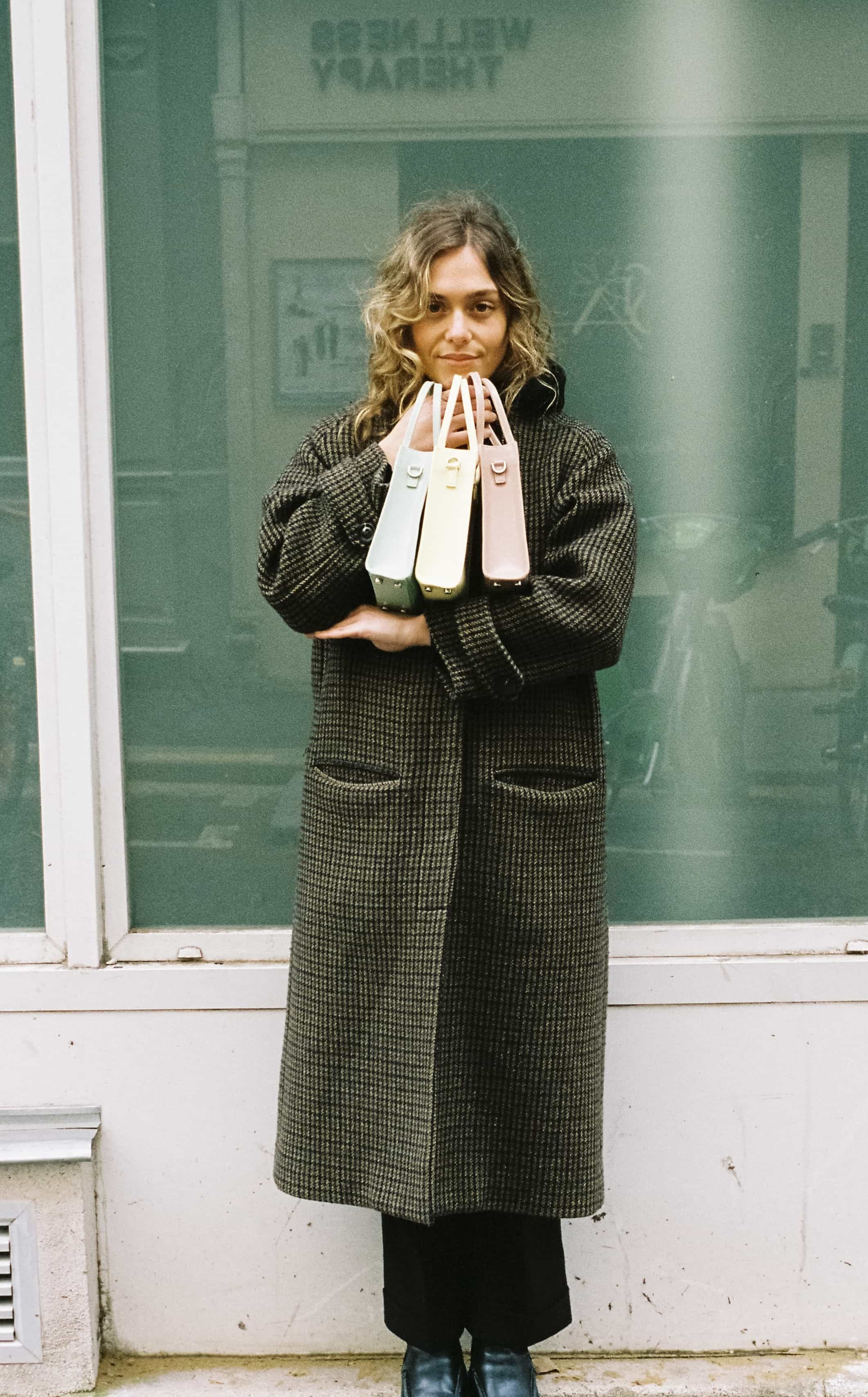 Femme en manteau tenant trois sacs pastel devant une vitrine