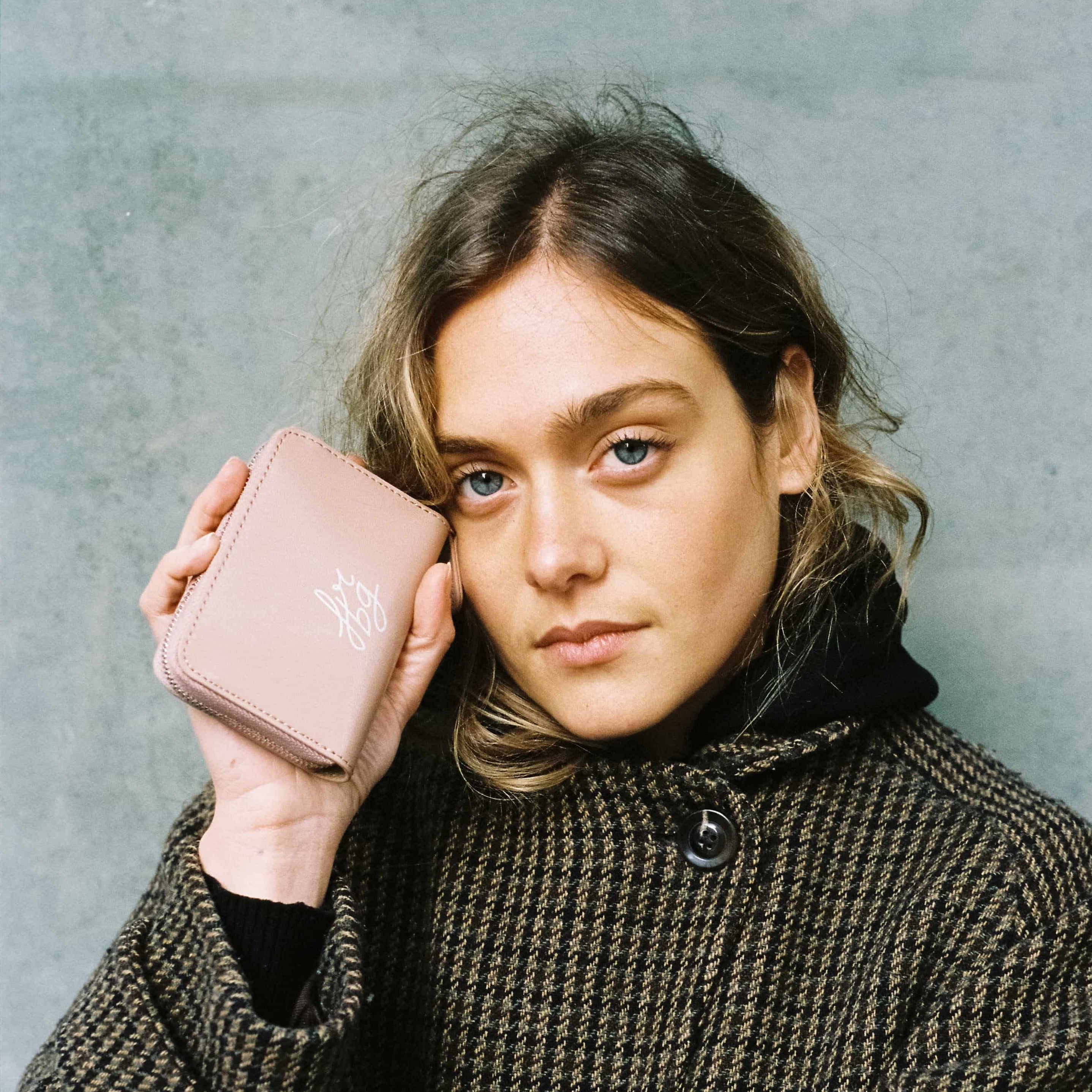 Femme en manteau à carreaux tenant un porte-monnaie rose clair près du visage