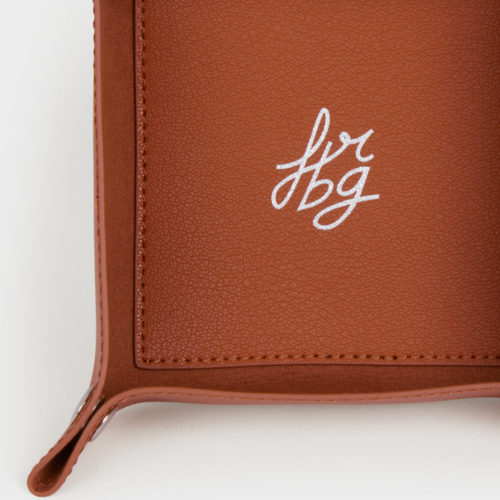 Détail d'un vide-poche en cuir marron clair avec logo argenté "fbg"